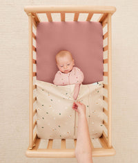 Baby lying in a bassinet under an ergoPouch HugMe Blanket in Daisy Sprinkle