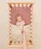 Baby lying in a bassinet under an ergoPouch HugMe Blanket in Daisy Sprinkle