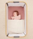Newborn baby asleep in a bedside sleeper under a ergoPouch HugMe Blanket in Caramel Grid