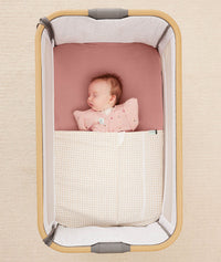Newborn baby asleep in a bedside sleeper under a ergoPouch HugMe Blanket in Caramel Grid