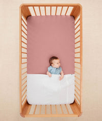 Baby lying in a crib under an ergoPouch HugMe Blanket in Midnight Stripe