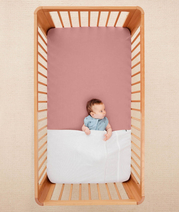 Baby lying in a crib under an ergoPouch HugMe Blanket in Midnight Stripe