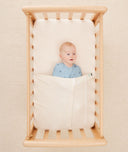 Newborn baby asleep in a bassinet under a ergoPouch HugMe Blanket in Caramel Grid