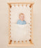 Newborn baby asleep in a bassinet under a ergoPouch HugMe Blanket in Caramel Grid