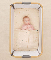 Baby lying in a bedside sleeper under an ergoPouch HugMe Blanket in Daisy Sprinkle