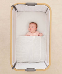 Baby lying in a bedside sleeper under an ergoPouch HugMe Blanket in Midnight Stripe