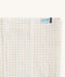 Close-up of a Newborn baby asleep in a bassinet under an ergoPouch HugMe Blanketin Caramel Grid displaying the 0.2 TOG side