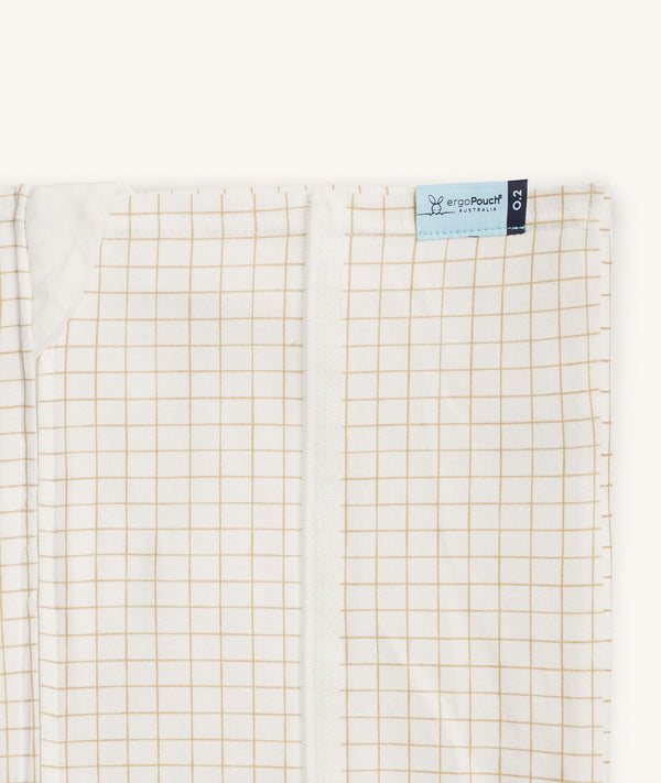 Close-up of a Newborn baby asleep in a bassinet under an ergoPouch HugMe Blanketin Caramel Grid displaying the 0.2 TOG side