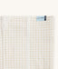Close-up of a Newborn baby asleep in a bassinet under an ergoPouch HugMe Blanketin Caramel Grid displaying the 0.2 TOG side