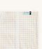 Close-up of a Newborn baby asleep in a bassinet under an ergoPouch HugMe Blanket in Caramel Grid displaying the 1.0 TOG side