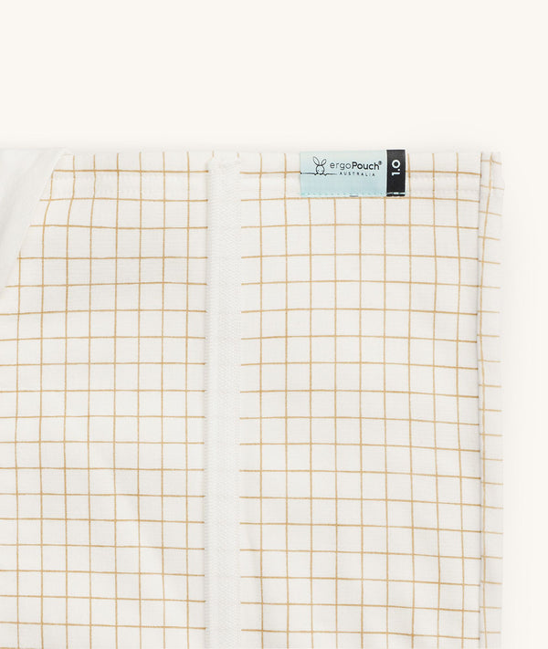 Close-up of a Newborn baby asleep in a bassinet under an ergoPouch HugMe Blanket in Caramel Grid displaying the 1.0 TOG side