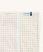 Close-up of a Newborn baby asleep in a bassinet under an ergoPouch HugMe Blanket in Caramel Grid displaying the 1.0 TOG side