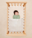 Baby asleep in a bassinet under an ergoPouch HugMe Blanket in Midnight Stripe