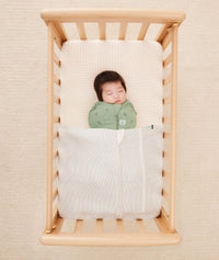Baby asleep in a bassinet under an ergoPouch HugMe Blanket in Midnight Stripe