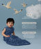 Infant wearing a ergoPouch Sleep Sack 1.0 TOG Starbeam with text about its features on a blue background with swans and clouds.