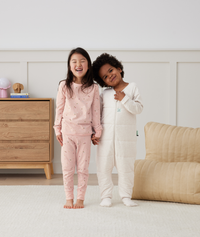 Two children in ergoPouch warm sleepwear; one in two-piece pajamas in Daisies, and the other in Sleep Onesie 2.5 TOG Oatmeal Marle