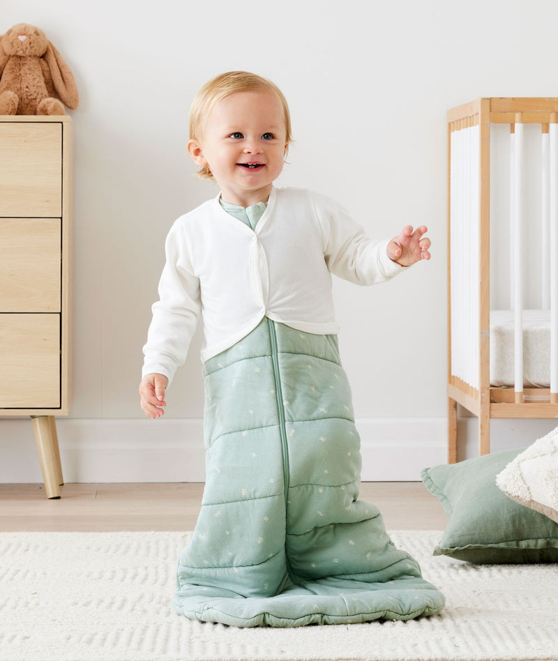 Infant standing smiling wearing a winter ergoPouch Sleeping Sack with the added layer of Arm Warmers