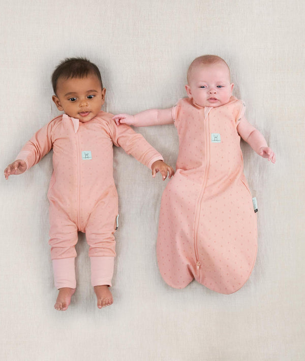 Two newborns lying wearing ergoPouch Long Sleeve Romper 1.0 TOG Berries and Cocoon Swaddle Sack 1.0 TOG Berries