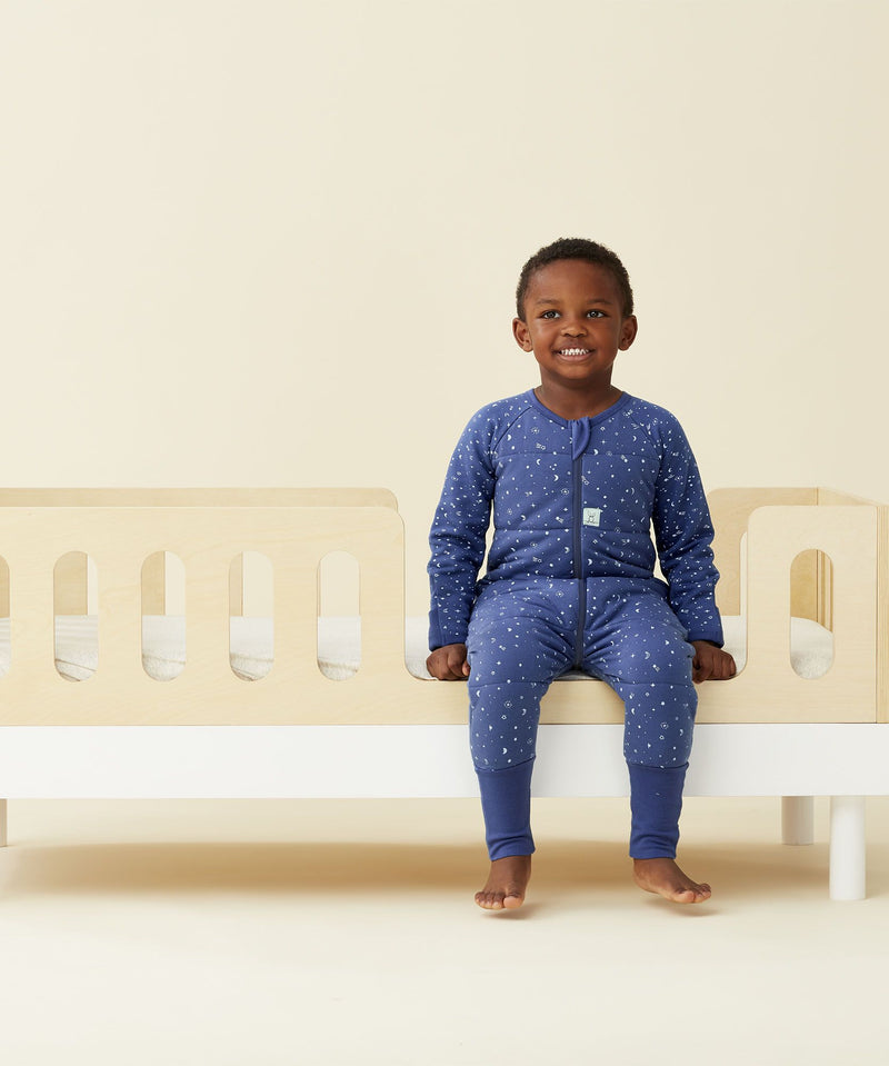 A cosy child smiling wearing a ergoPouch Sleep Onesie 2.5 TOG Night Sky
