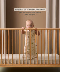 Infant standing inside the ergoPouch ellska Skye Crib, made from non-toxic beechwood to be safe from curious hands and mouths.