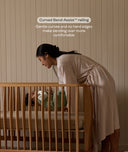 Woman placing baby into the ergoPouch ellska Skye Crib, supported by ergonomic Bend-Assist™ railings for easier access