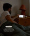Man sitting in bed using the ergoPouch Drift Home Baby Monitor and Smart TOG Guide to check on the his child