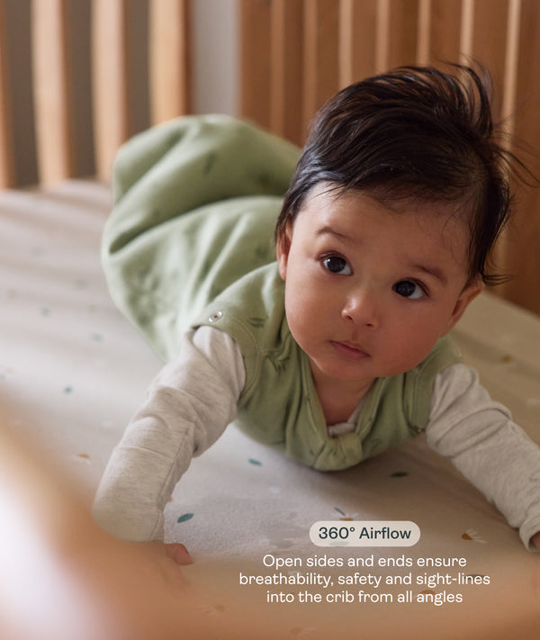 Baby lying on stomach in the ergoPouch ellska Skye Crib with an open side, providing breathability, safety, and clear sight-lines from every angle.