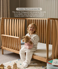 Toddler sitting on the ergoPouch ellska Skye Crib converted into a toddler bed, supporting a smooth big-bed transition.