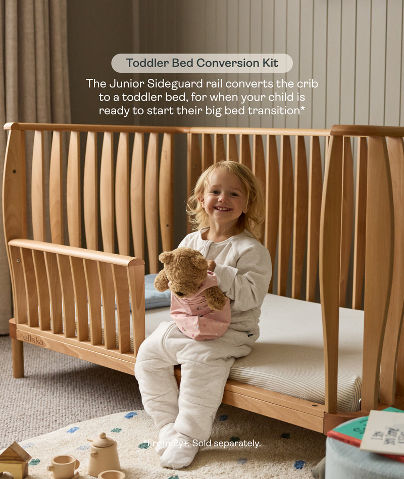 Toddler sitting on the ergoPouch ellska Skye Crib converted into a toddler bed, supporting a smooth big-bed transition.