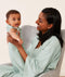 Mom wearing an ergoPouch Matchy Matchy Robe Sage, sitting and holding baby