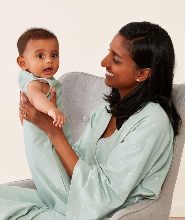 Mom wearing an ergoPouch Matchy Matchy Robe Sage, sitting and holding baby