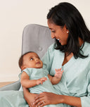 Mom wearing an ergoPouch Matchy Matchy Robe Sage, sitting and holding baby