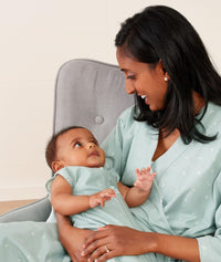 Mom wearing an ergoPouch Matchy Matchy Robe Sage, sitting and holding baby