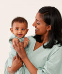 Mom wearing an ergoPouch Matchy Matchy Robe Sage, standing and holding baby