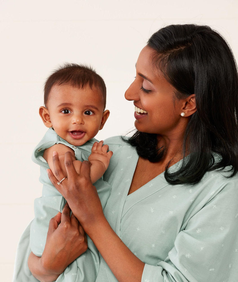 Mom wearing an ergoPouch Matchy Matchy Robe Sage, standing and holding baby