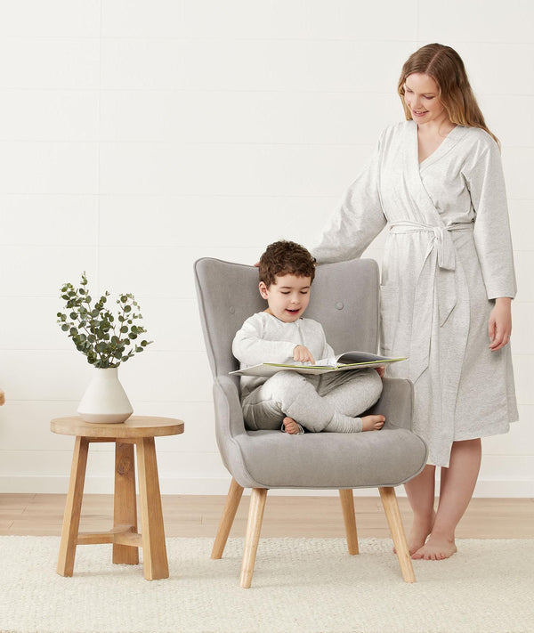 Mom wearing a an ergoPouch Matchy Matchy Robe Grey Marle, smiling down at child reading in a matching color Sleep Onesie