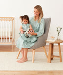 Mom wearing a an ergoPouch Matchy Matchy Robe Sage, smiling down at child reading in a matching color Sleep Suit Sack