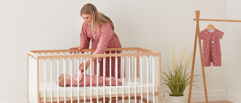 Mom reaching down into crib to hold baby's hand