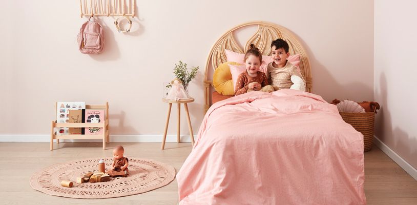 Two toddlers sitting in big bed together with pink ergoPouch bedding