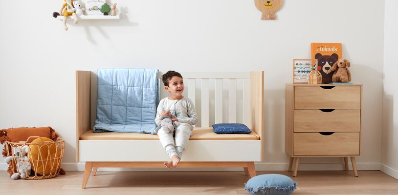 Boy sitting on his crib with one side down to begin mimicking the experience of a big bed before the transition from crib to bed
