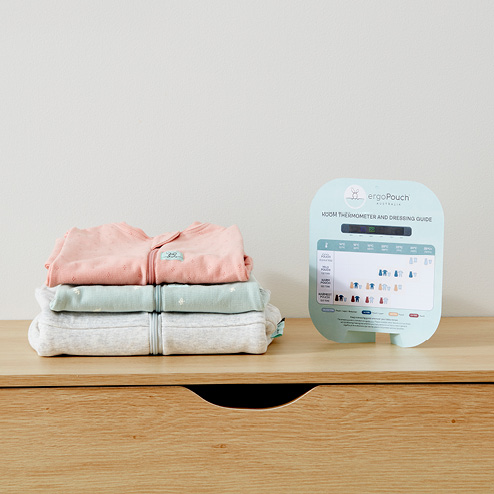 Baby winter sleepwear stacked on top of each other next to a ergoPouch Room Thermometer