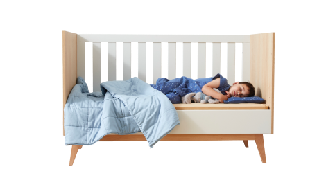 Toddler sleeping in cot with blanket and pillow